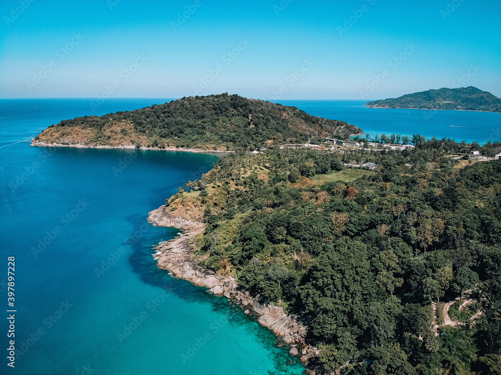 Top view of a coast of a huge uninhabited island covered with dense wild forest, around which the blue sea