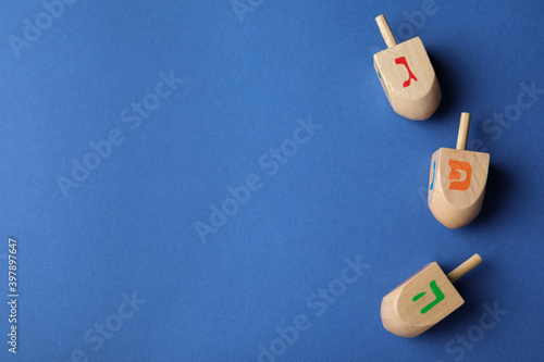 Hanukkah traditional dreidels with letters Gimel, Pe and He on blue background, flat lay. Space for text photo