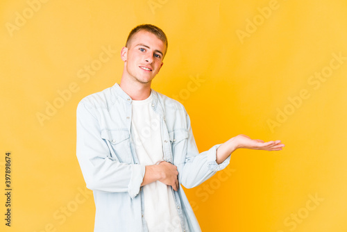 Young caucasian handsome man showing a copy space on a palm and holding another hand on waist.