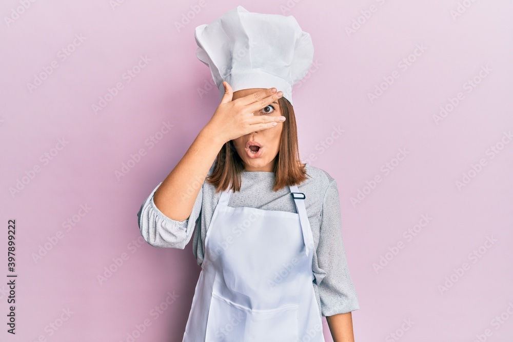 Young beautiful woman wearing professional cook uniform and hat peeking in shock covering face and eyes with hand, looking through fingers with embarrassed expression. Young beautiful woman wearing professional cook uniform and hat peeking in shock covering face and eyes with hand, looking through fingers with embarrassed expression.
