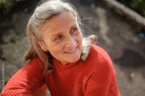 Close up portrait of a smiling senior woman with grey hair and face with wrinkles outdoors relaxing at park during sunny day