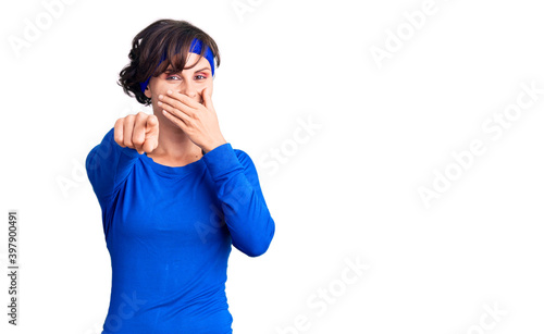 Beautiful young woman with short hair wearing training workout clothes laughing at you, pointing finger to the camera with hand over mouth, shame expression