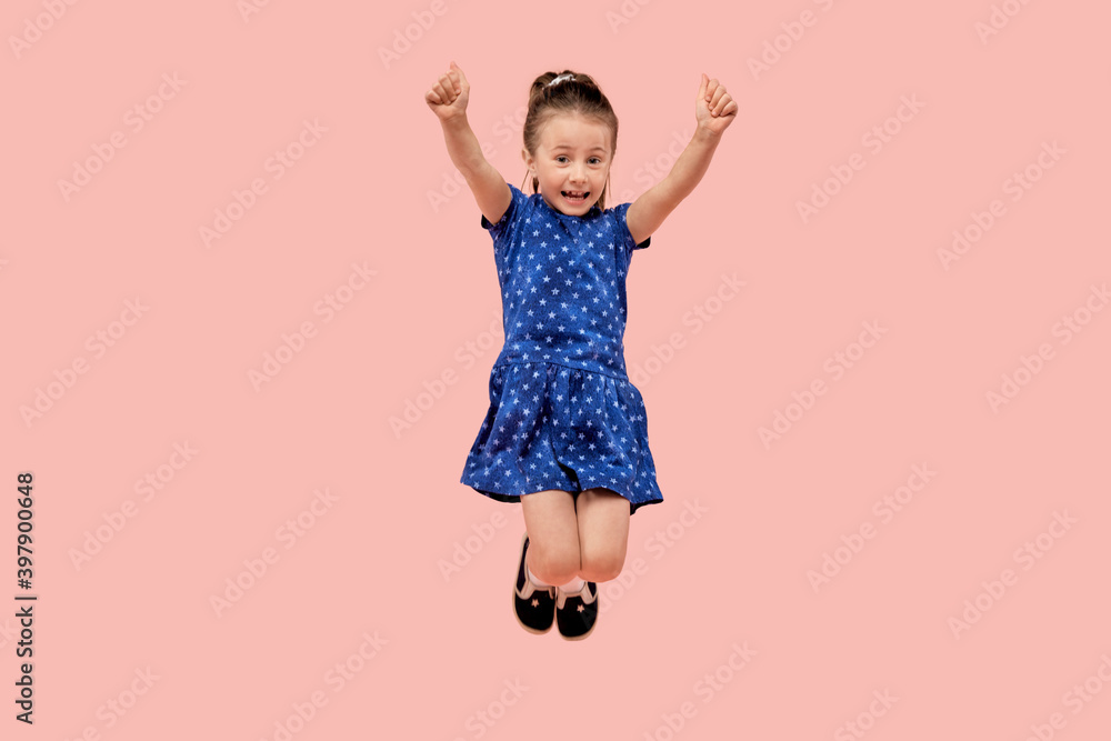 A happy child rejoices in victory with his hands raised up and jumps up. The concept of winning. Human emotion. In a blue dress with a small star print. Pink isolated background. A happy child rejoices in victory with his hands raised up and jumps up. The concept of winning. Human emotion. In a blue dress with a small star print. Pink isolated background.