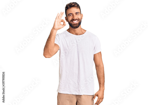 Young hispanic man wearing casual white tshirt smiling positive doing ok sign with hand and fingers. successful expression.