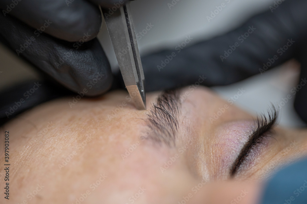 Obraz premium Stylist working on an eyebrow with a tweezers.
