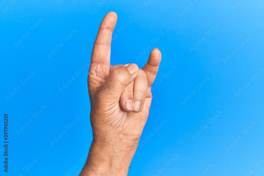 Hand of senior hispanic man over blue isolated background gesturing rock and roll symbol, showing obscene horns gesture Hand of senior hispanic man over blue isolated background gesturing rock and roll symbol, showing obscene horns gesture