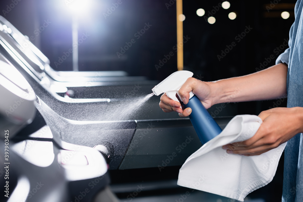 Obraz premium partial view of charwoman holding rag while spraying cleanser on treadmill in gym on blurred foreground