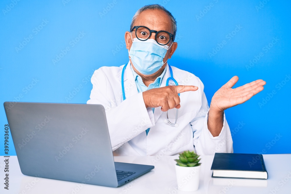 Senior handsome man with gray hair wearing doctor uniform and medical mask amazed and smiling to the camera while presenting with hand and pointing with finger. Senior handsome man with gray hair wearing doctor uniform and medical mask amazed and smiling to the camera while presenting with hand and pointing with finger.