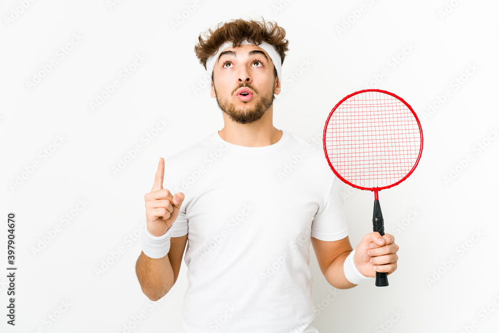 Young indian man playing badminton pointing upside with opened mouth. Young indian man playing badminton pointing upside with opened mouth.