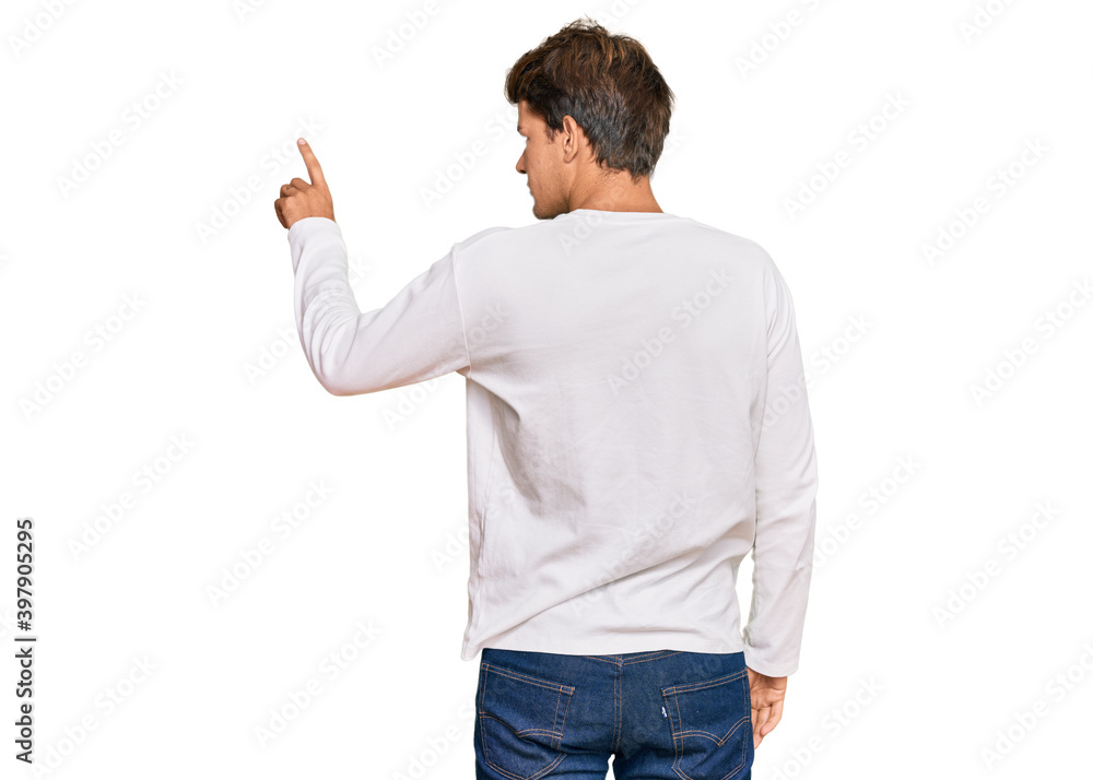 Handsome caucasian man wearing casual white sweater posing backwards pointing ahead with finger hand Handsome caucasian man wearing casual white sweater posing backwards pointing ahead with finger hand