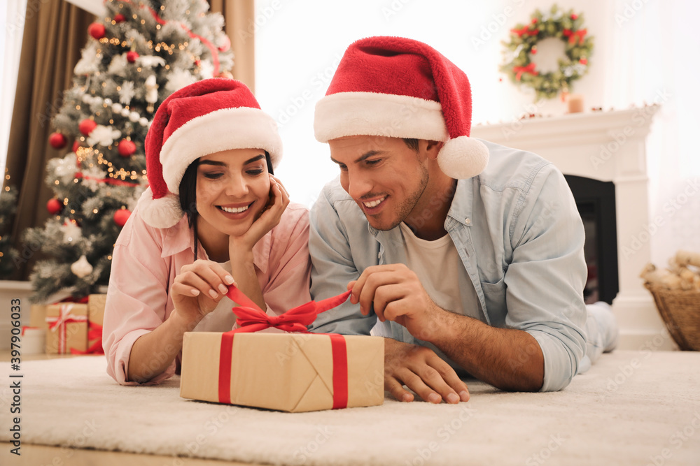 Happy couple in Santa hats with Christmas gift at home Happy couple in Santa hats with Christmas gift at home