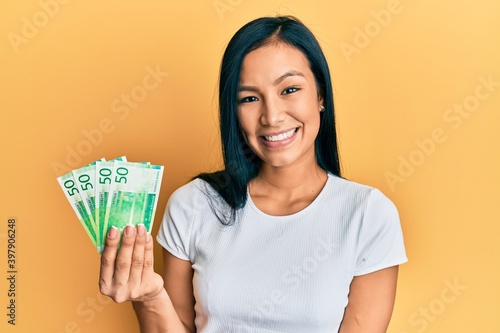 Beautiful hispanic woman holding 50 norwegian krone banknotes looking positive and happy standing and smiling with a confident smile showing teeth