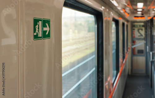 Aisle of train next to coupe cabins, blurred landscape behind window, shallow depth of field photo, focus on green emergency exit sign at wall