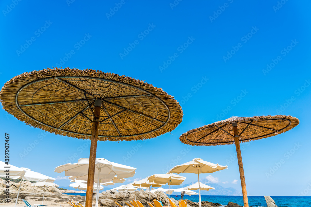 Rows of yellow beach umbrellas and sun beds on the white sand close to the crystal clear waster of Mediterranean sea. Ideal 5 star blue flag beach in Greece, Halkidiki. Tourist paradise. 