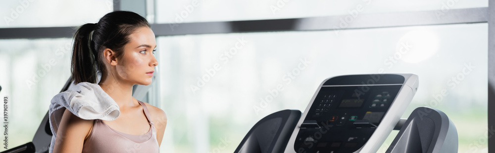 young sportswoman with towel looking away while standing on treadmill, banner young sportswoman with towel looking away while standing on treadmill, banner