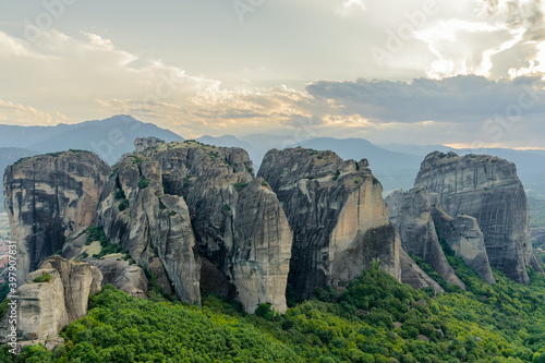 Meteora rock formation in Greece . Unique and enormous columns of rock rising high lit by rays of settin sun at the sunset and with dramatic clouds above. Amazing place 