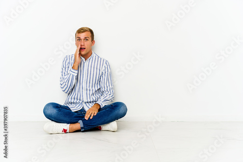 Young caucasian man sitting on the floor shouts loud, keeps eyes opened and hands tense. © Asier
