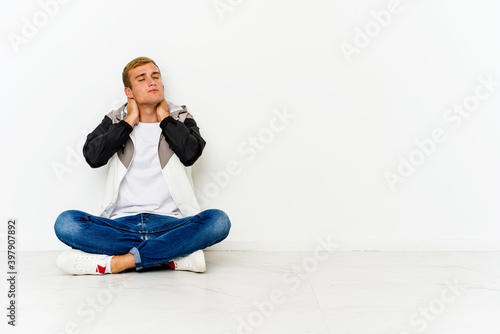 Young caucasian man sitting on the floor suffering neck pain due to sedentary lifestyle.