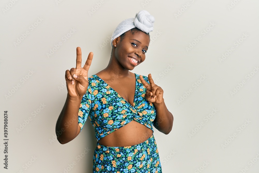 Young african woman wearing hair turban and african style smiling looking to the camera showing fingers doing victory sign. number two. Young african woman wearing hair turban and african style smiling looking to the camera showing fingers doing victory sign. number two.