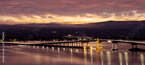 Long duration exposure of the sunrise breaking over the tops of nearby mountains, and leaving a brilliant streak of light along the bridge deck. © Walt