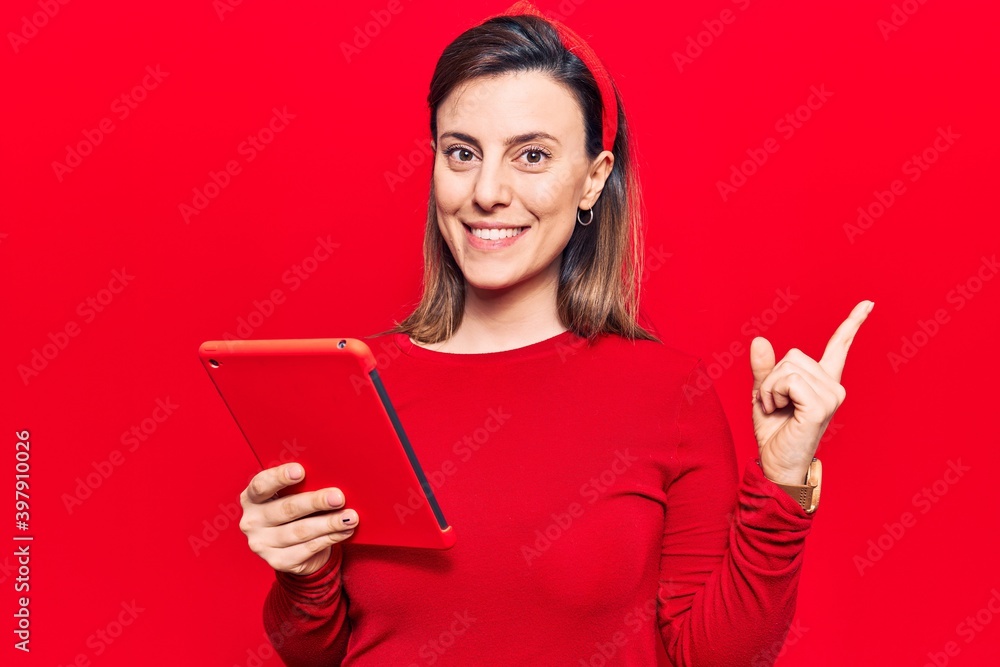 Young beautiful woman holding touchpad smiling happy pointing with hand and finger to the side Young beautiful woman holding touchpad smiling happy pointing with hand and finger to the side