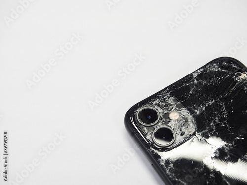 The back of modern black smartphone with a broken glass and a damaged curved body close-up isolated on white background