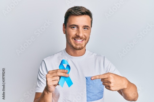 Handsome caucasian man holding blue ribbon smiling happy pointing with hand and finger