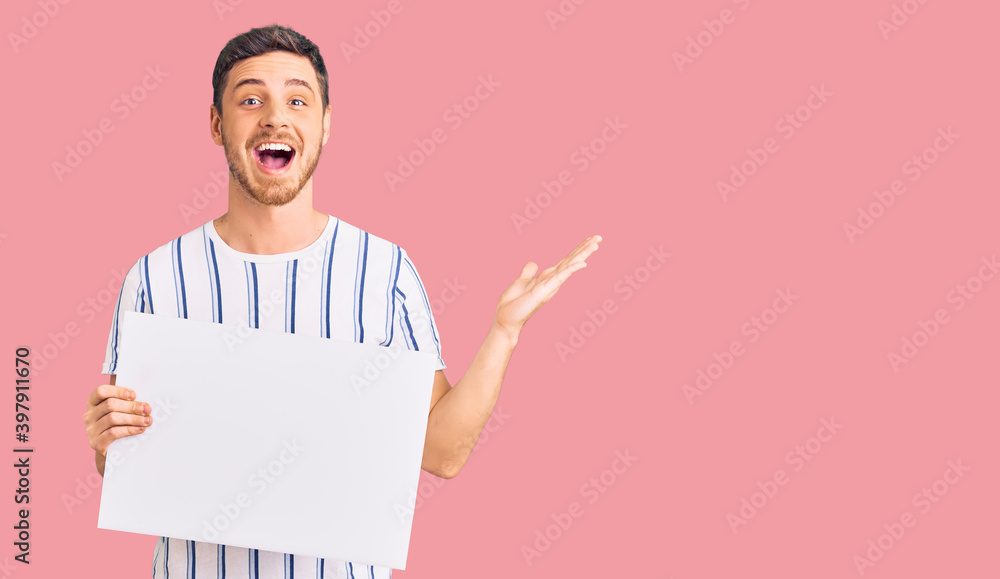 Handsome young man with bear holding blank empty banner celebrating victory with happy smile and winner expression with raised hands Handsome young man with bear holding blank empty banner celebrating victory with happy smile and winner expression with raised hands