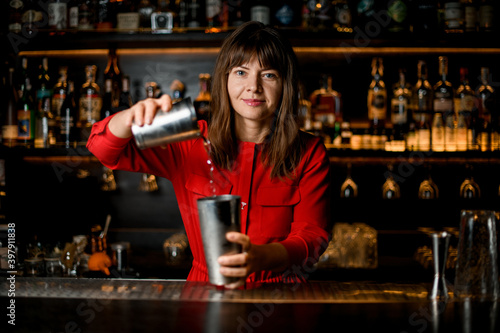 focus on face of woman bartender holding shaker glasses and pouring liquid
