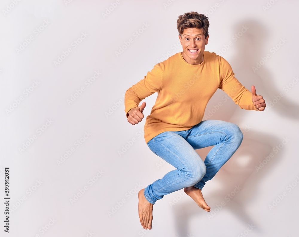 Young handsome man wearing casual clothes smiling happy. Jumping with smile on face doing ok sing with thumbs up over isolated white background