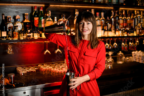 beautiful smiling woman bartender in red dress prepares cocktail