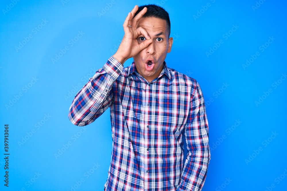 Young handsome latin man wearing casual clothes doing ok gesture shocked with surprised face, eye looking through fingers. unbelieving expression.