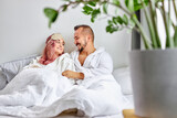 young couple relax on bed together, at weekends. caucasian married couple in bathrobes are in love, in light bedroom