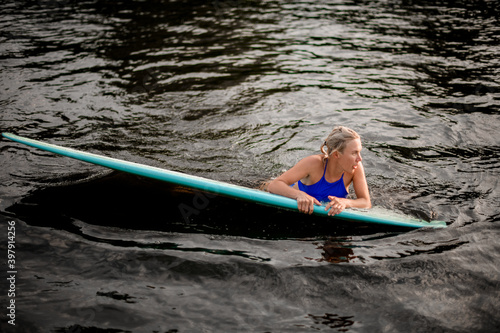 young blonde woman swims on the water leaning on bright surf board.