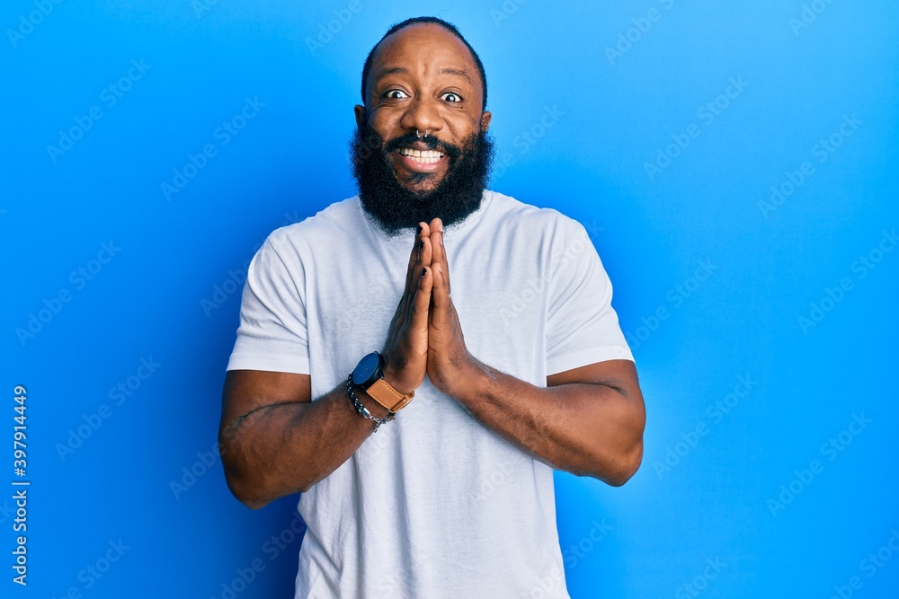Young african american man wearing casual white tshirt praying with hands together asking for forgiveness smiling confident.