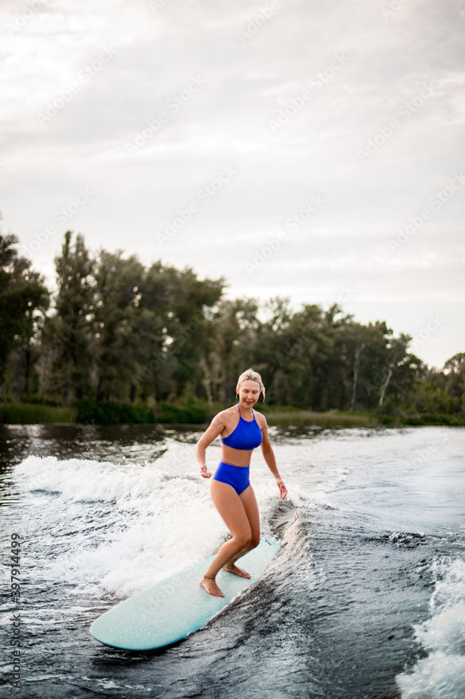 young blonde woman balances on surfboard while riding the wave. young blonde woman balances on surfboard while riding the wave.