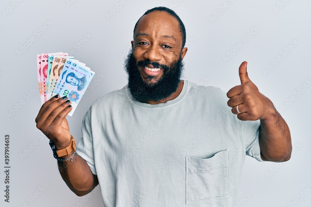 Young african american man holding yuan chinese banknotes smiling happy and positive, thumb up doing excellent and approval sign Young african american man holding yuan chinese banknotes smiling happy and positive, thumb up doing excellent and approval sign