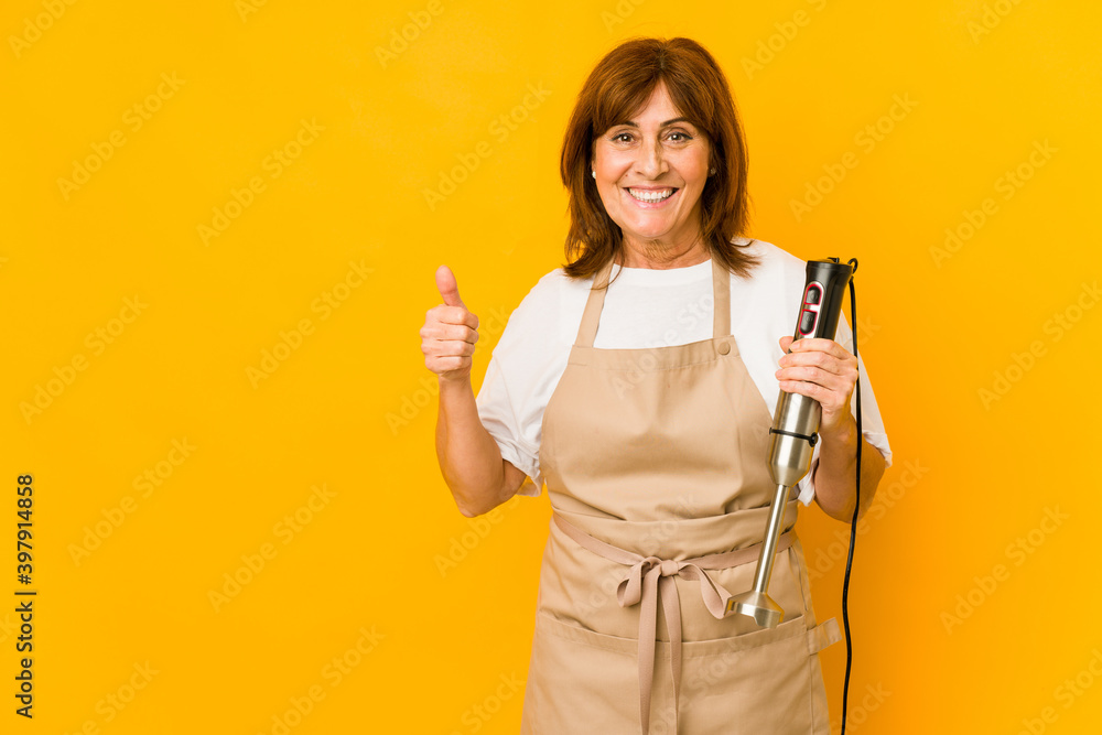 Middle age caucasian cook woman holding a mixer isolated smiling and raising thumb up Middle age caucasian cook woman holding a mixer isolated smiling and raising thumb up
