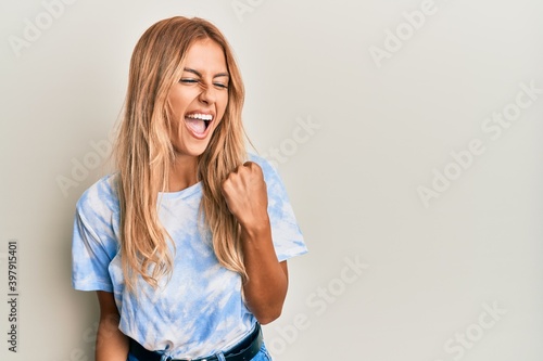 Beautiful blonde young woman wearing tye die tshirt celebrating surprised and amazed for success with arms raised and eyes closed
