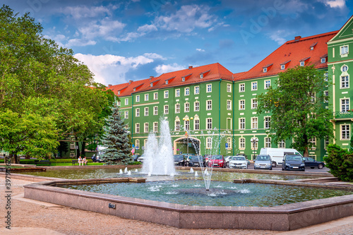 Green buildings of Szczecin City Council with red rooftops. Fountains in a pond and green trees on Jasne Blonia square, Stettin, Poland