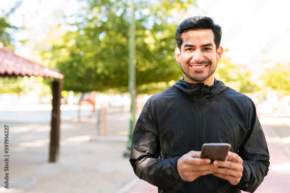 Sporty man making eye contact and smiling with his smartphone Sporty man making eye contact and smiling with his smartphone