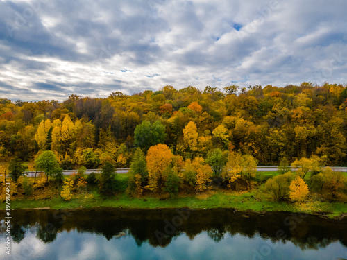 Aerial autumn view of a hill with golden trees and reflections in river