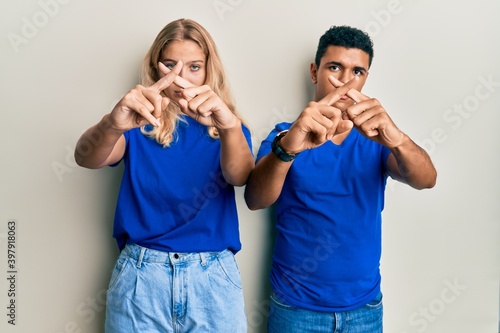 Young interracial couple wearing casual clothes rejection expression crossing fingers doing negative sign