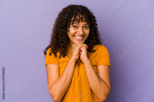 Young african american afro woman isolated keeps hands under chin, is looking happily aside.