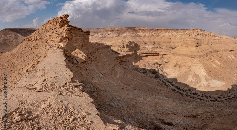 A picturesque panoramic view on a dry riverbed Hatira, Israel. Orange sandy mountains and white clouds on a blue sky. Typical landscape with dry river bends and high mountain slopes in Negev desert.