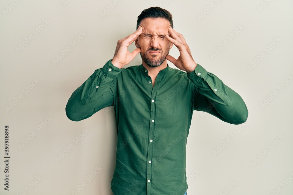 Handsome man with beard wearing casual clothes with hand on head, headache because stress. suffering migraine. Handsome man with beard wearing casual clothes with hand on head, headache because stress. suffering migraine.