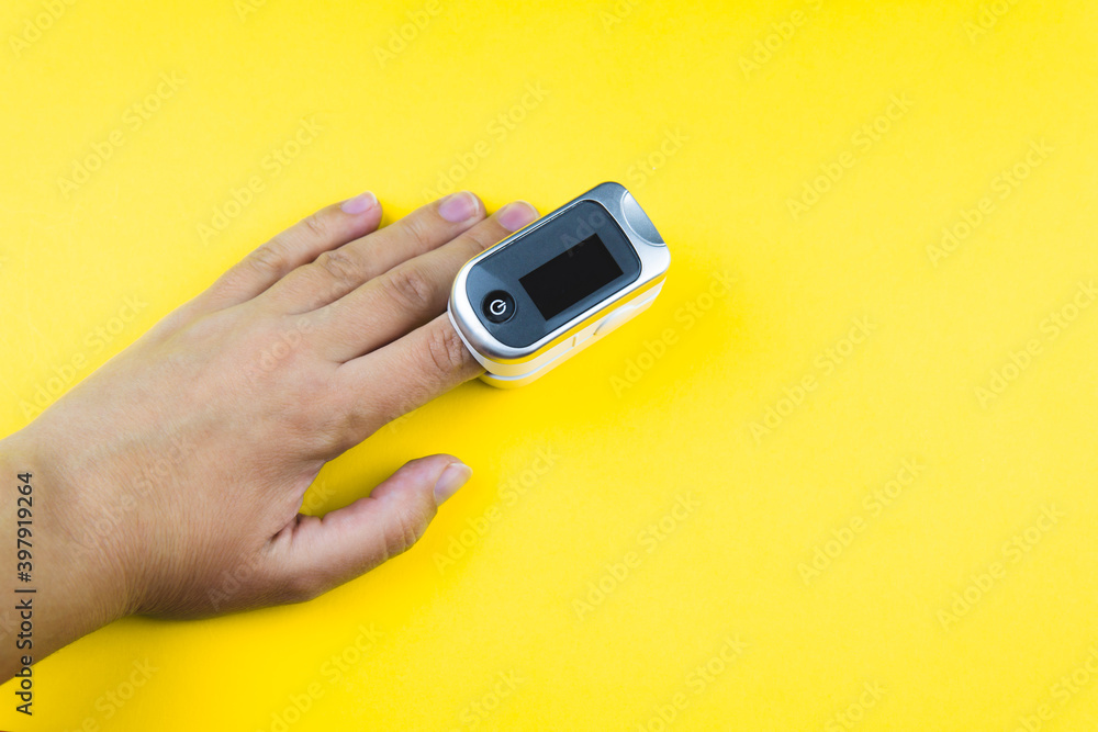 Woman hand with a finger in pulse oximeter on yellow background. Self monitoring and protection during epidemic concept. Copy space. Woman hand with a finger in pulse oximeter on yellow background. Self monitoring and protection during epidemic concept. Copy space.
