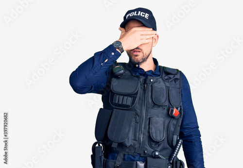Young handsome man wearing police uniform covering eyes with hand, looking serious and sad. sightless, hiding and rejection concept
