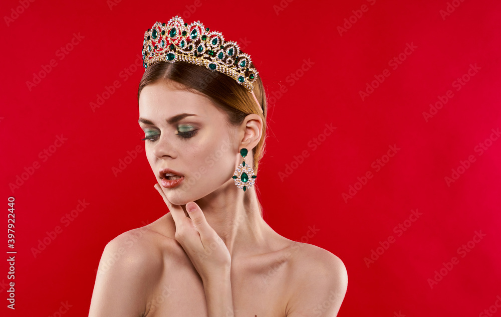 Portrait of a confident woman on a red background with a crown on her head and earrings on her ears Portrait of a confident woman on a red background with a crown on her head and earrings on her ears