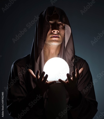 фотографія Young wizard with crystal ball in dark room